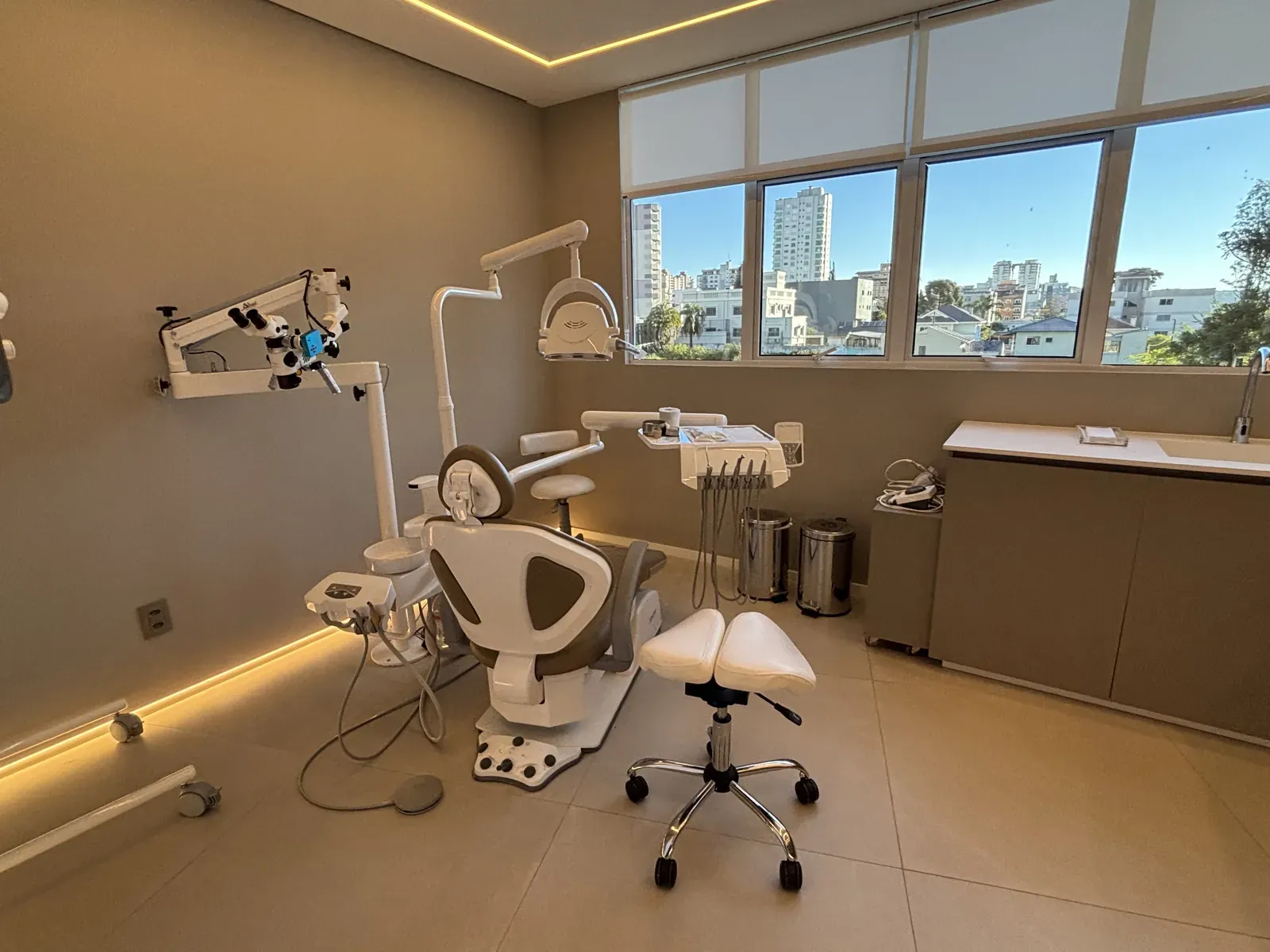 Consultório da LINEARE com o microscópio odontológico ao lado da cadeira e as janelas ao fundo.